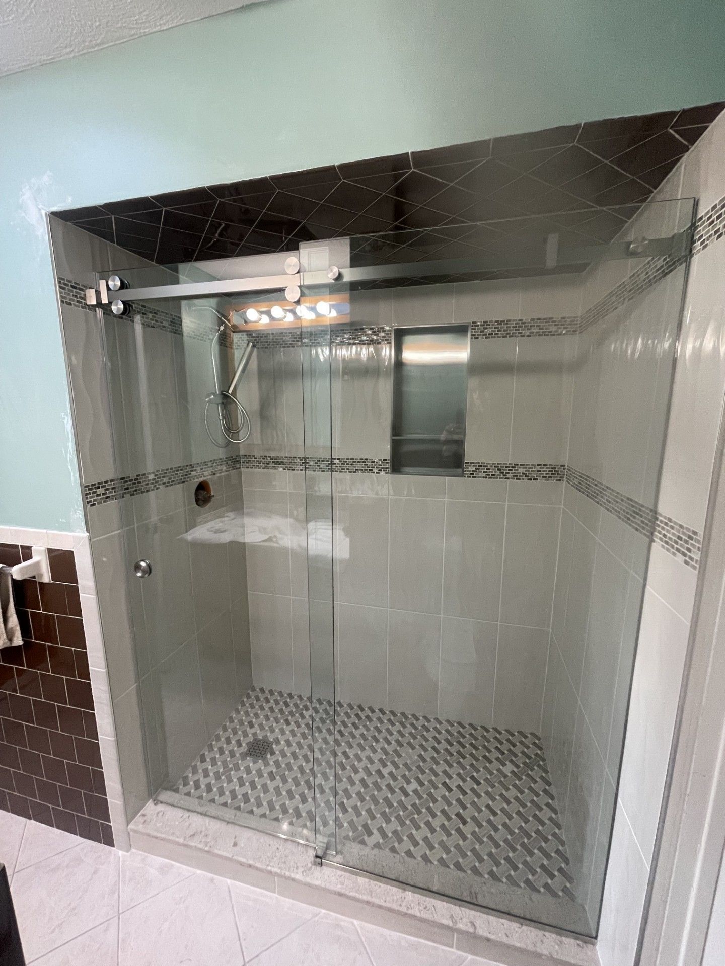 Glass shower enclosure with gray and white tile, a dark ceiling, and a patterned floor.