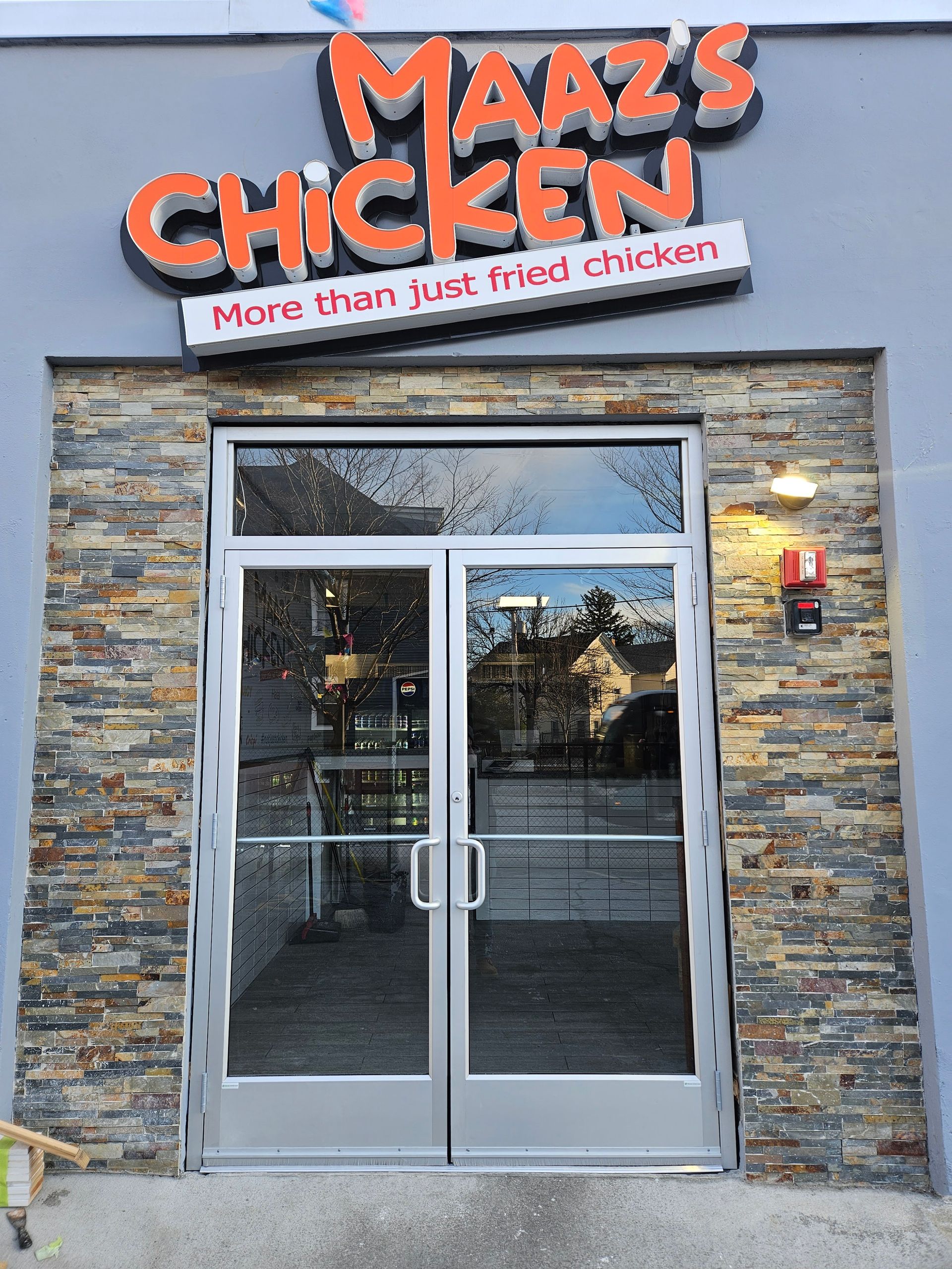 Maaz's Chicken restaurant entrance with sign above double doors, stone facade, and reflective glass.