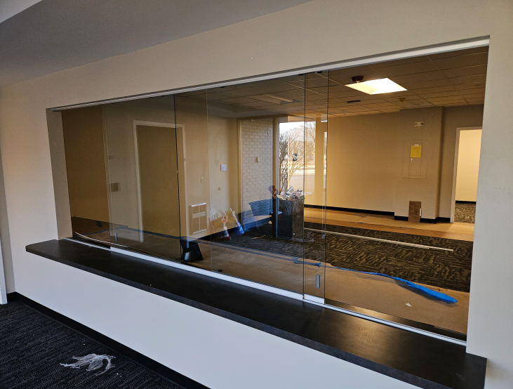 Glass partition in a room, with a black countertop and a view of another room; unfinished.