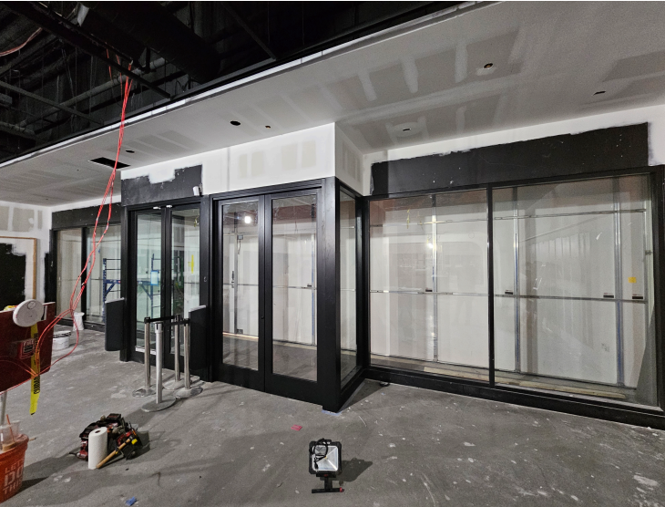 Storefront under construction, featuring black framed glass doors and windows, unfinished walls, and construction equipment.