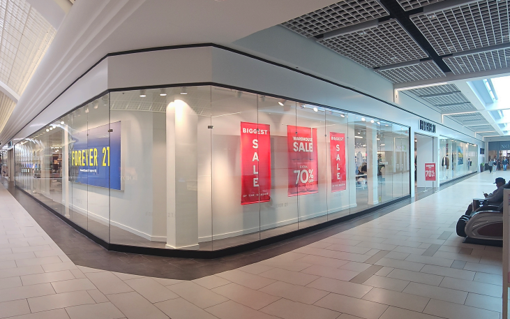 Mall storefronts, including Forever 21, with sale signs; a person sits in a motorized chair.