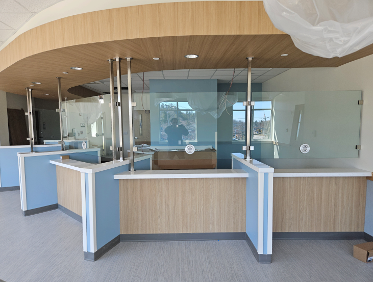 Reception area with light blue and wood-tone counters and glass dividers. Curved ceiling.