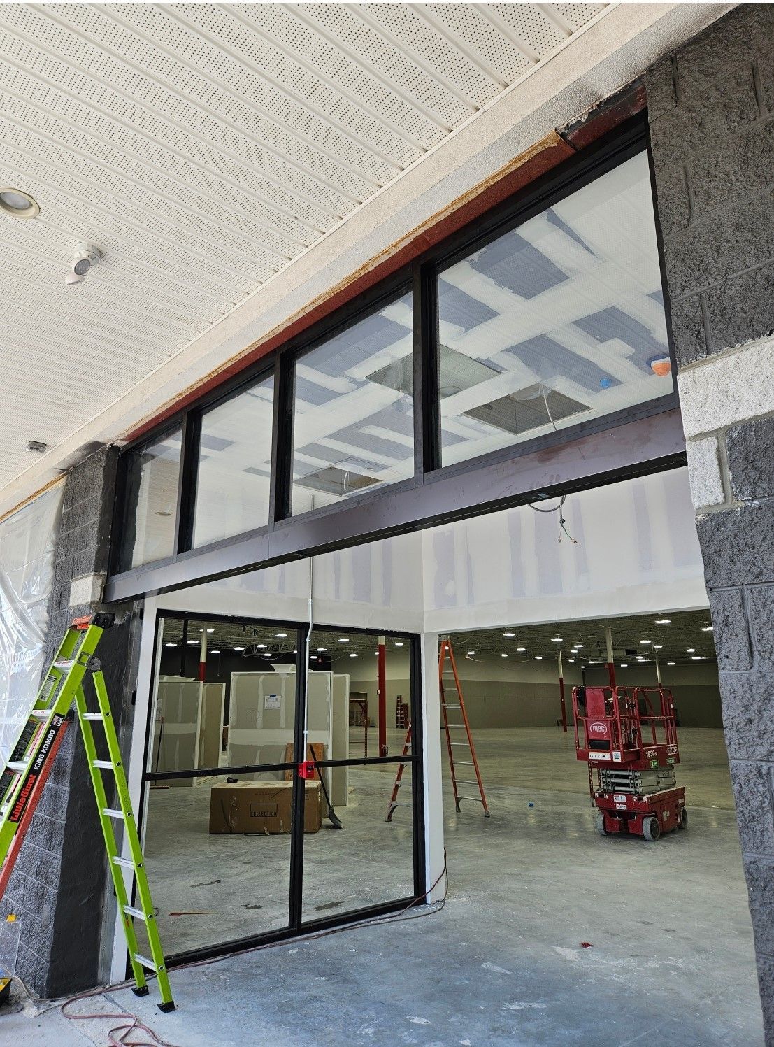 Exterior of a building under construction, featuring glass windows, a doorway, and construction equipment.