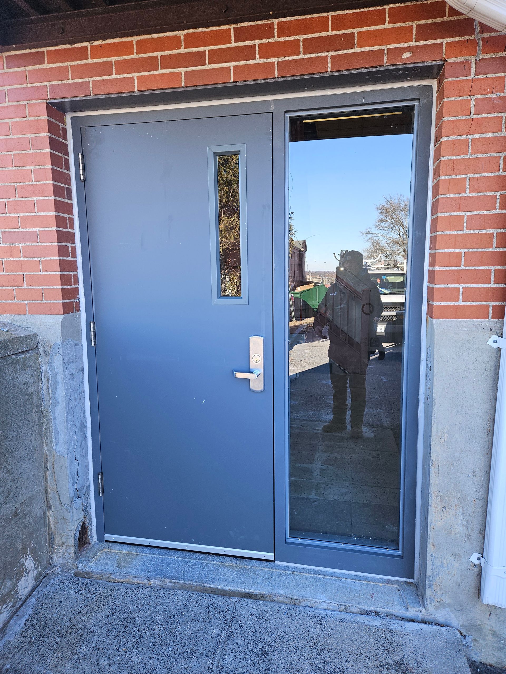 Blue door with glass panel on brick building. Person reflected in glass.