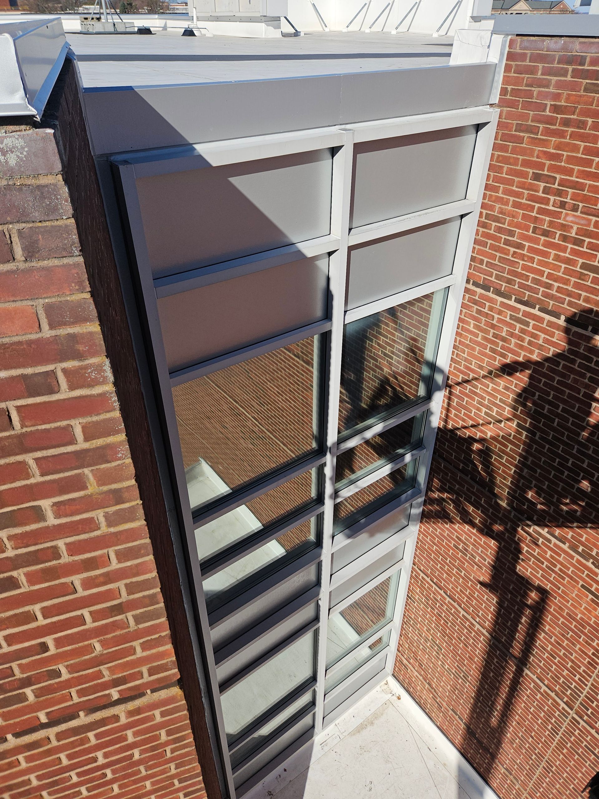 Tall, narrow window with gray frame and glass panels set in a brick wall. Sunlight casts shadows.