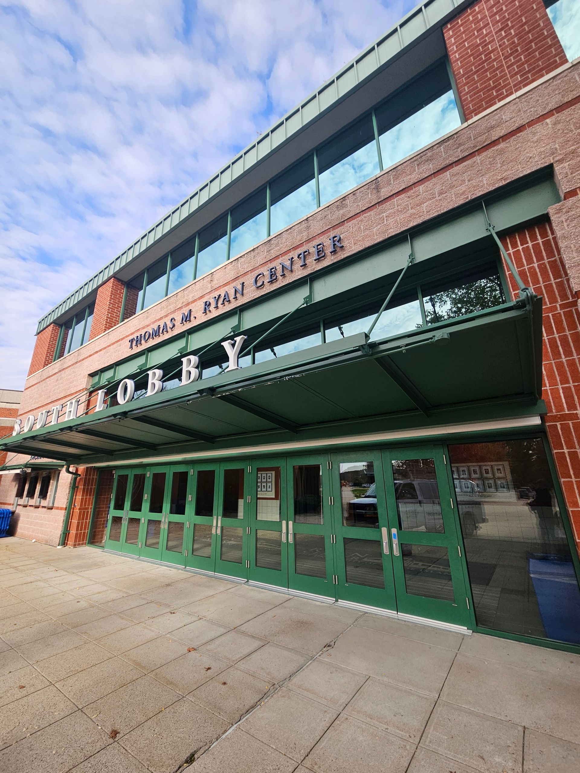 Exterior of the Thomas M. Ryan Center with a green awning and doors, red brick, and blue sky.