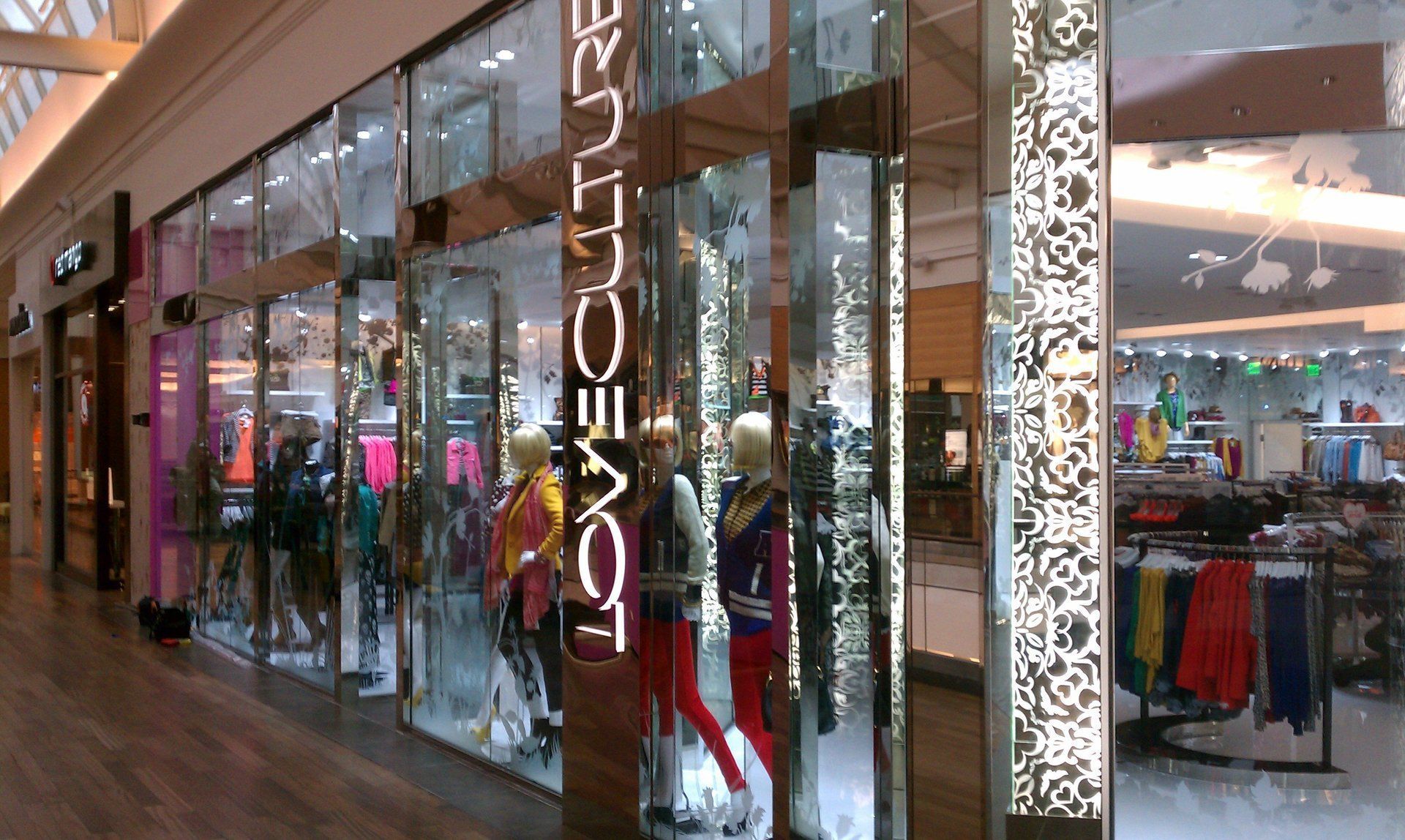 Clothing store exterior with mannequins in window displays; indoor shopping mall setting.