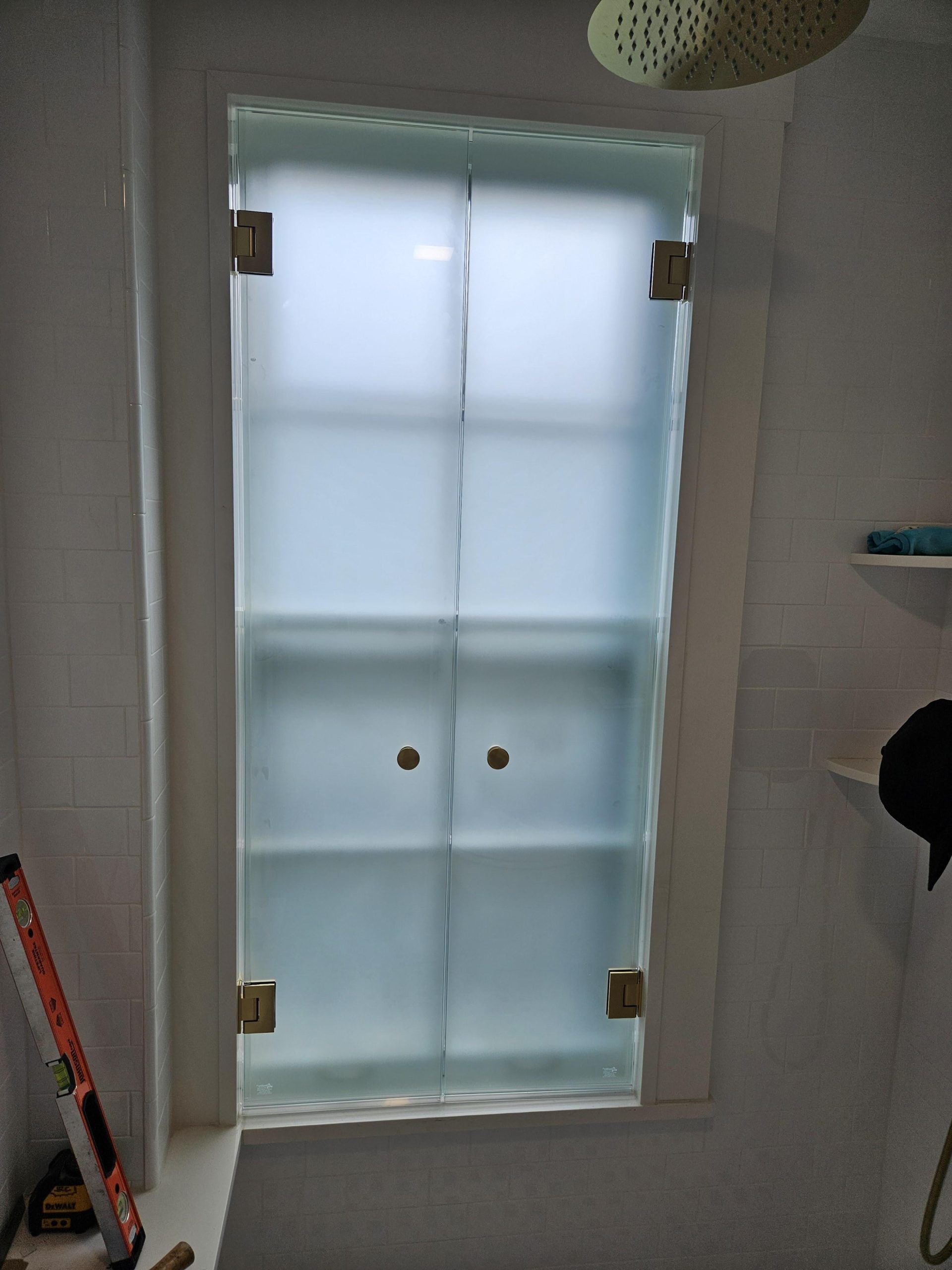 Frosted glass shower door with brass hinges in a white bathroom.