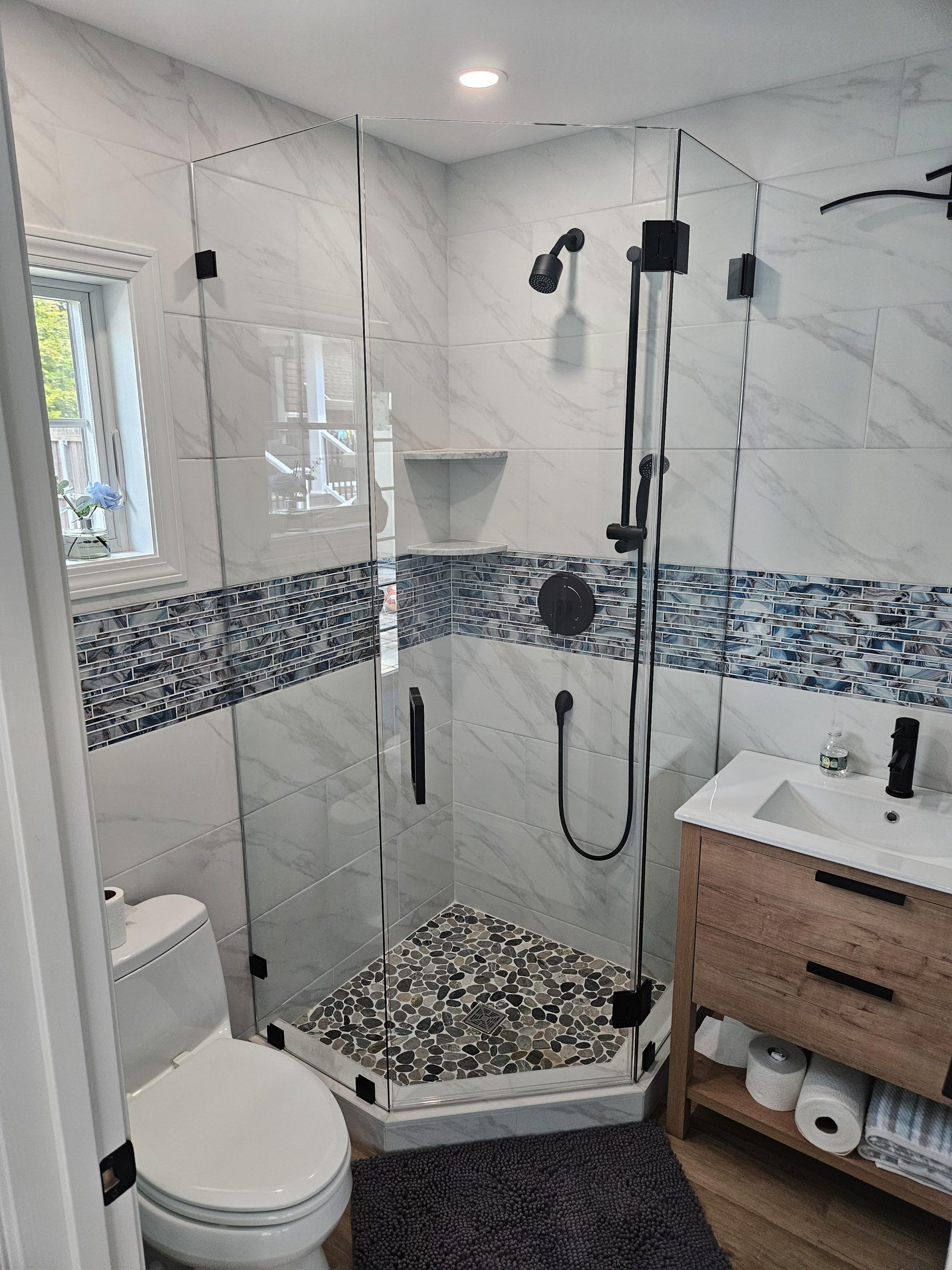 Modern bathroom with a glass-enclosed shower, wood vanity, and mosaic tile accents.