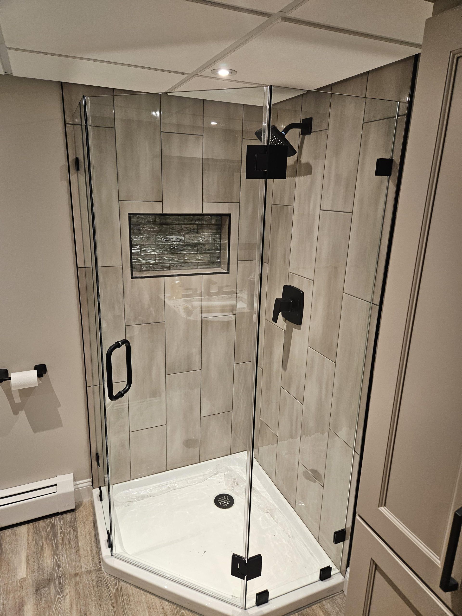Modern shower with glass doors, black fixtures, and light-colored tile walls.