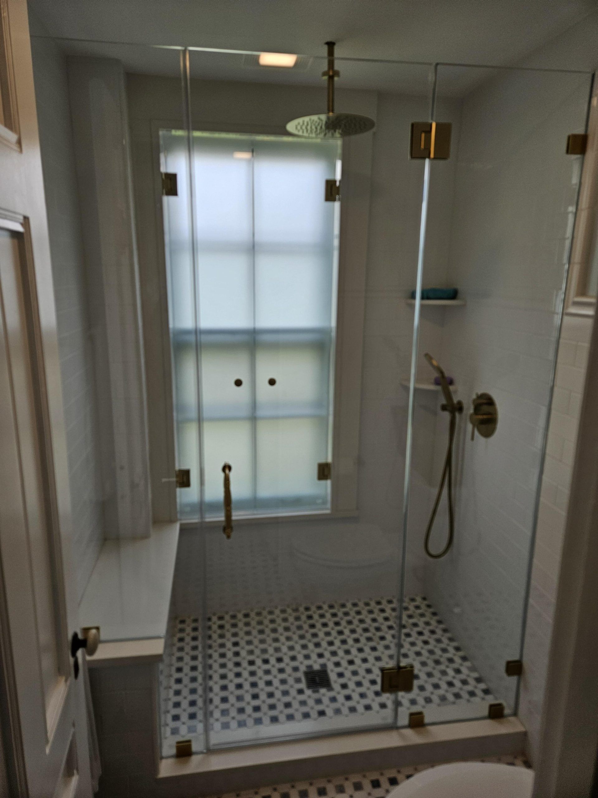 Glass shower with brass hardware; tiled floor with a window at the back.