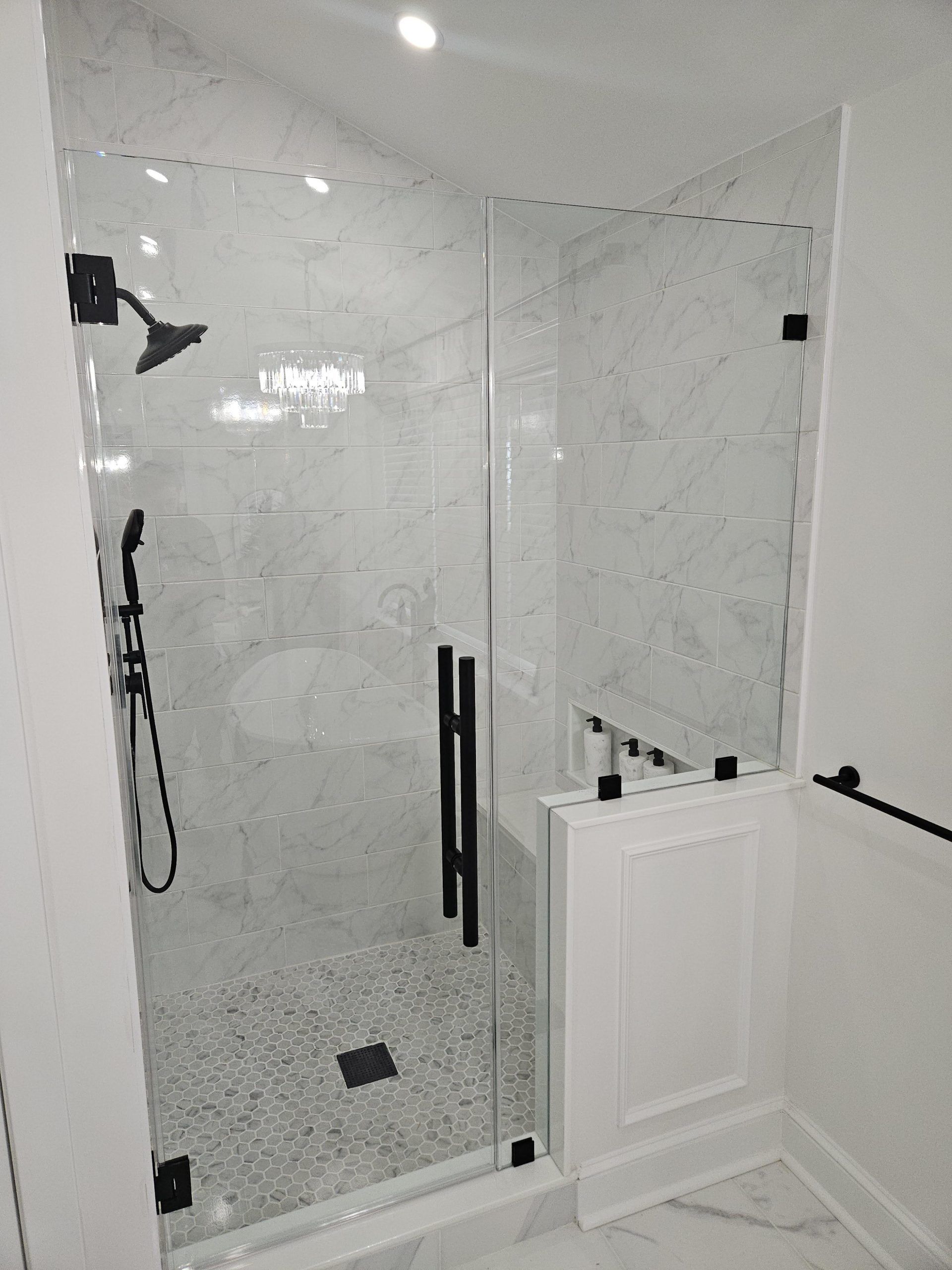 Modern shower with glass door, black fixtures, and white marble tile.
