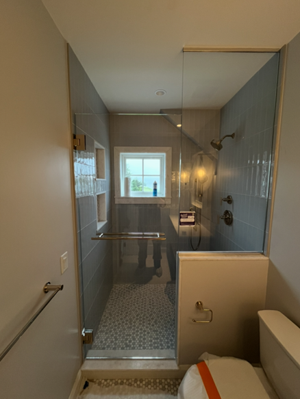 Shower with glass door, gray tile, pebble floor, and white toilet in a bathroom.