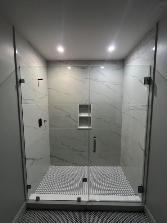 Glass shower enclosure with gray marble tile walls, mosaic floor, and two recessed shelves.