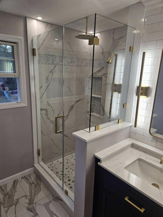 Modern shower with glass doors, gold hardware, marble tile, and a vanity.