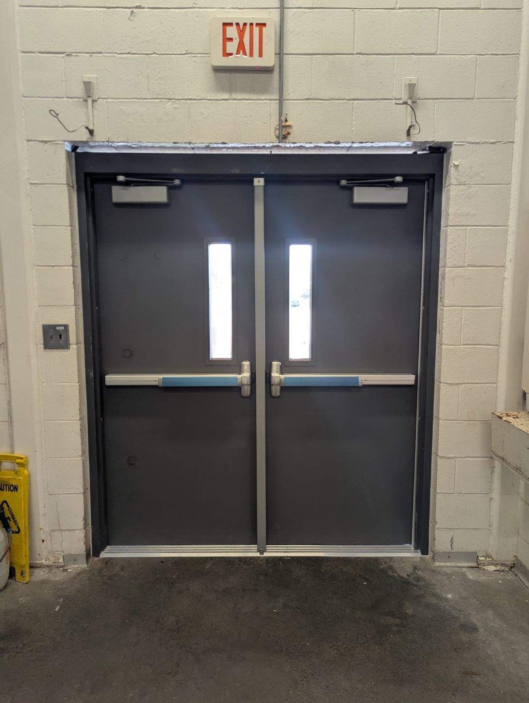 Double gray doors with blue push bars and rectangular windows, under an 