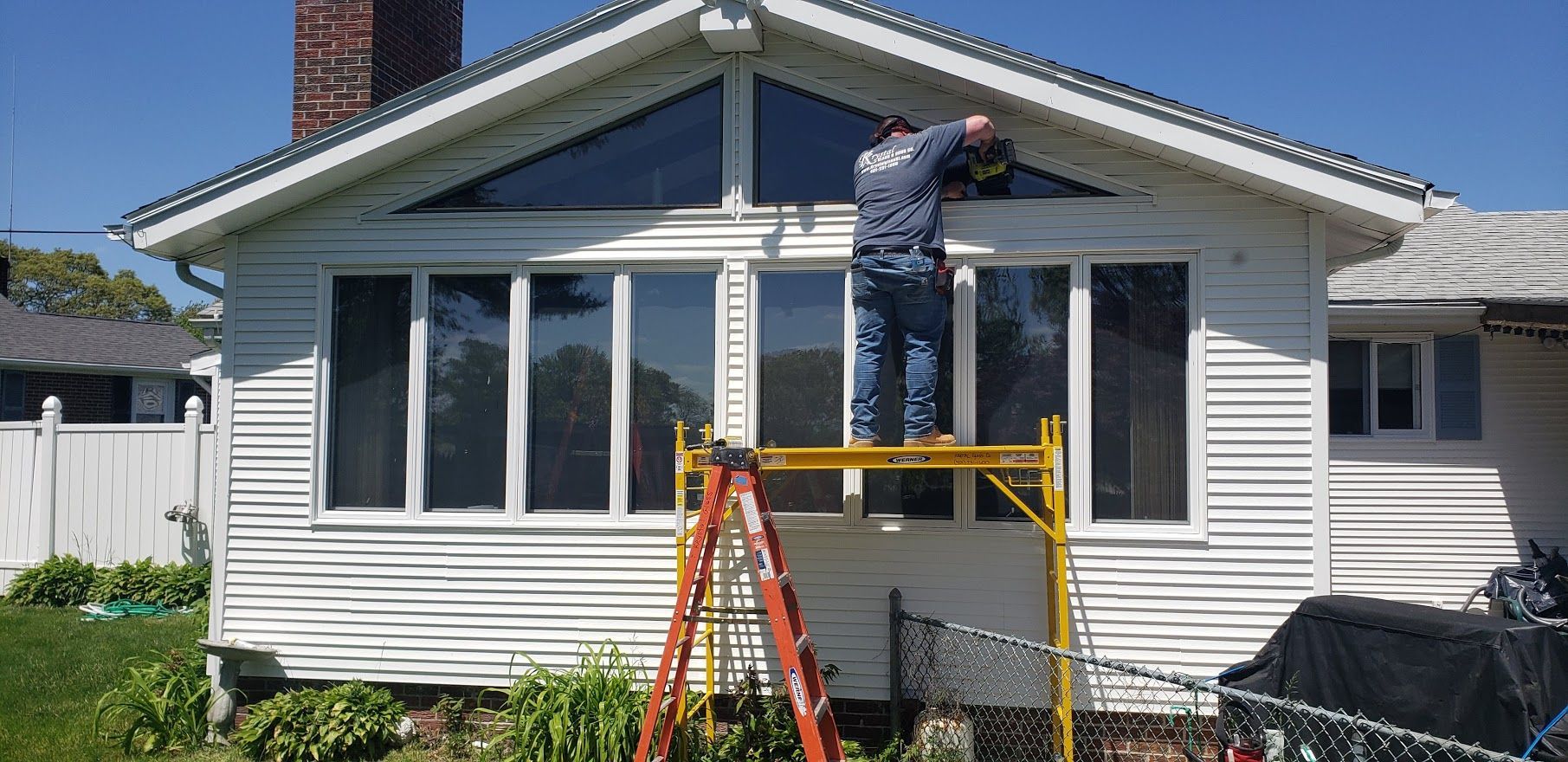 A person on scaffolding works on a home's exterior trim under the triangular window.