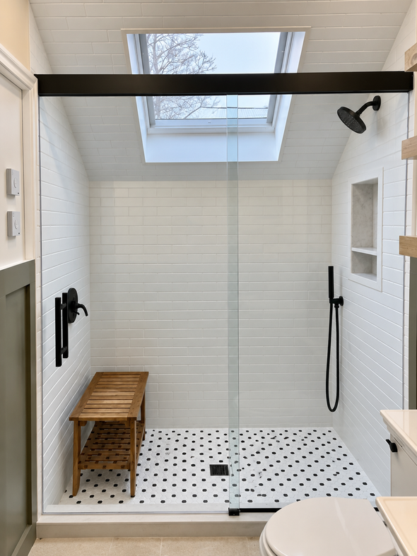 Modern walk-in shower with white tile, skylight, black fixtures, bench, and glass door