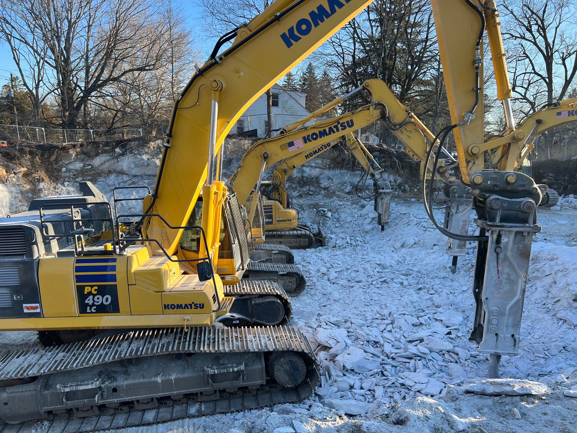 Yellow Komatsu excavators with jackhammers breaking concrete in a snowy construction site.