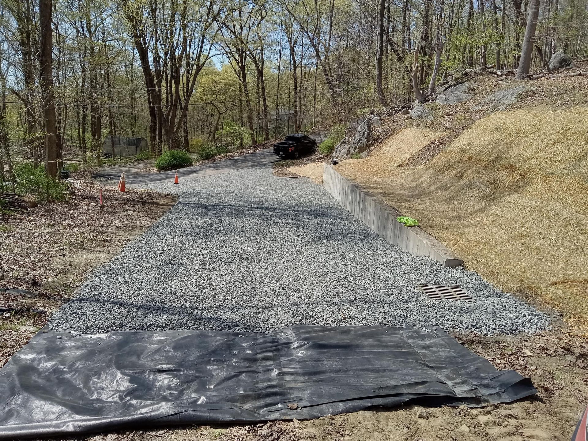 Gravel pathway under construction, bordered by a concrete wall and wood chips. Trees in the background.