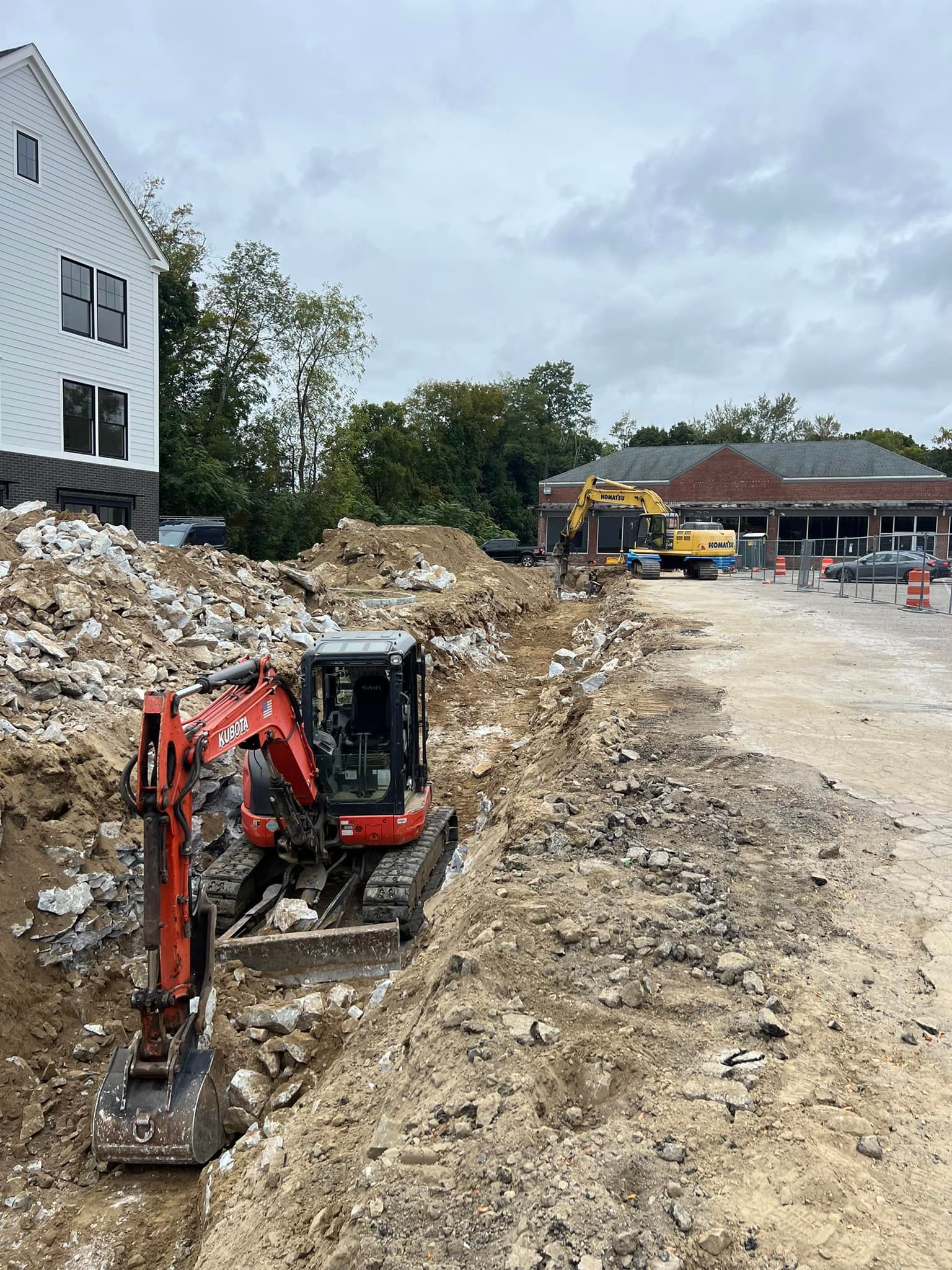 Construction site with excavator digging. Building and other machinery are visible.