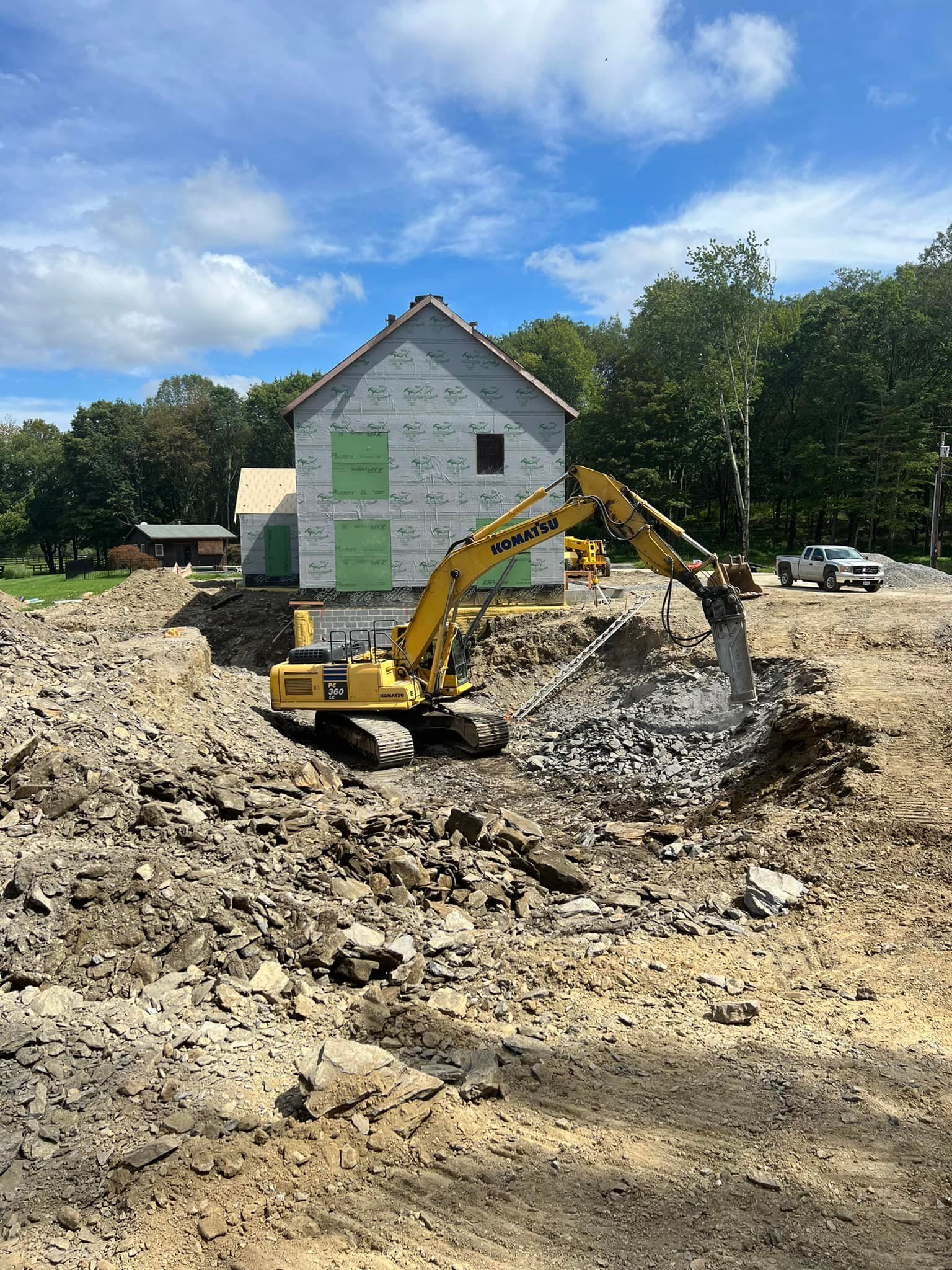 Excavator demolishes foundation of a house. Dirt and debris surround the construction site on a sunny day.