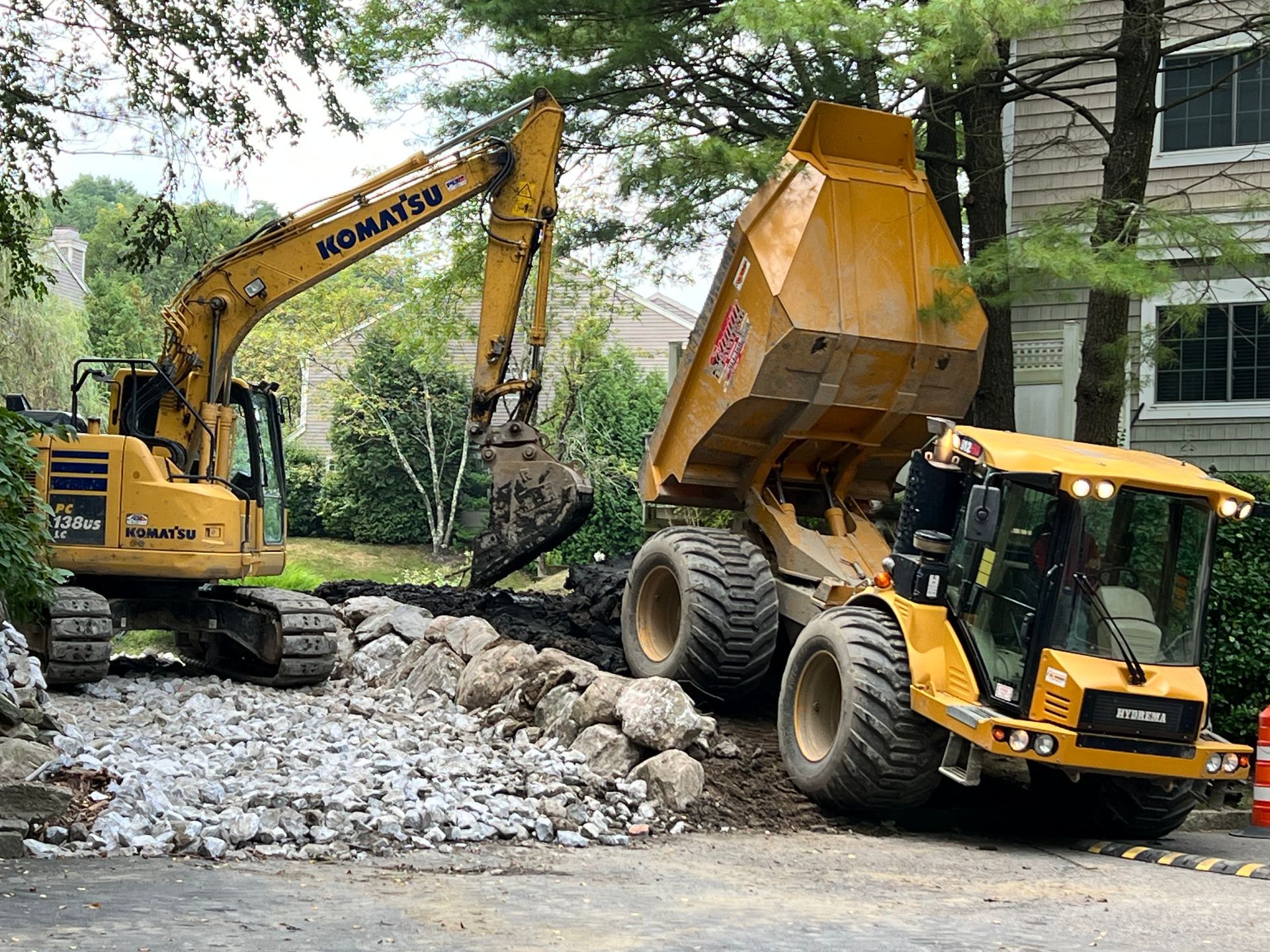 Yellow excavator loading dirt into yellow dump truck, working on a road.
