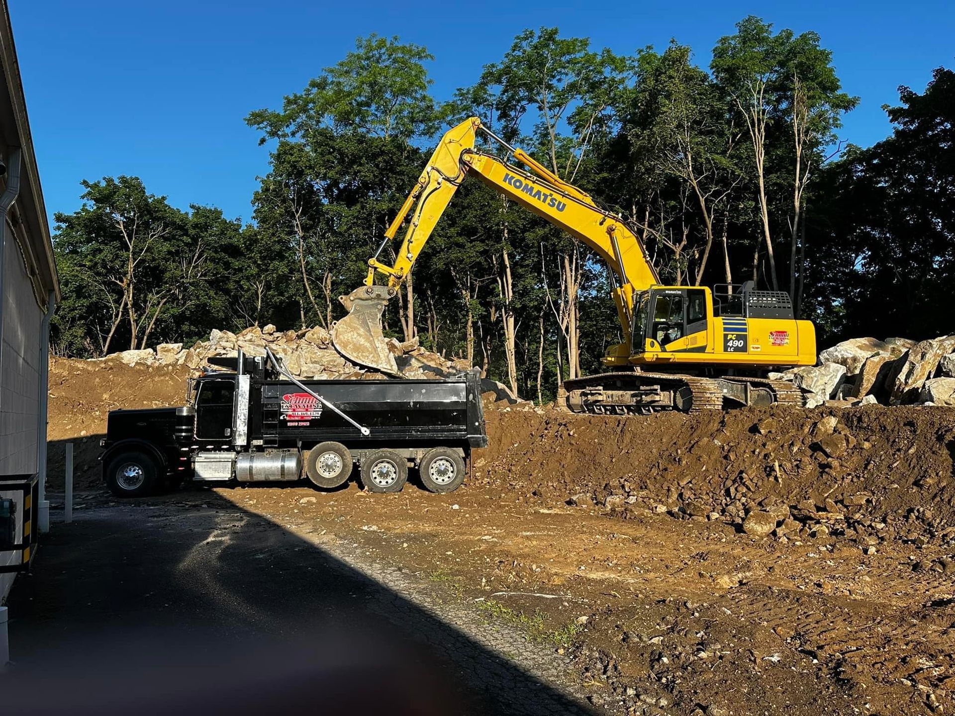 Yellow excavator loading a black dump truck with dirt on a construction site.