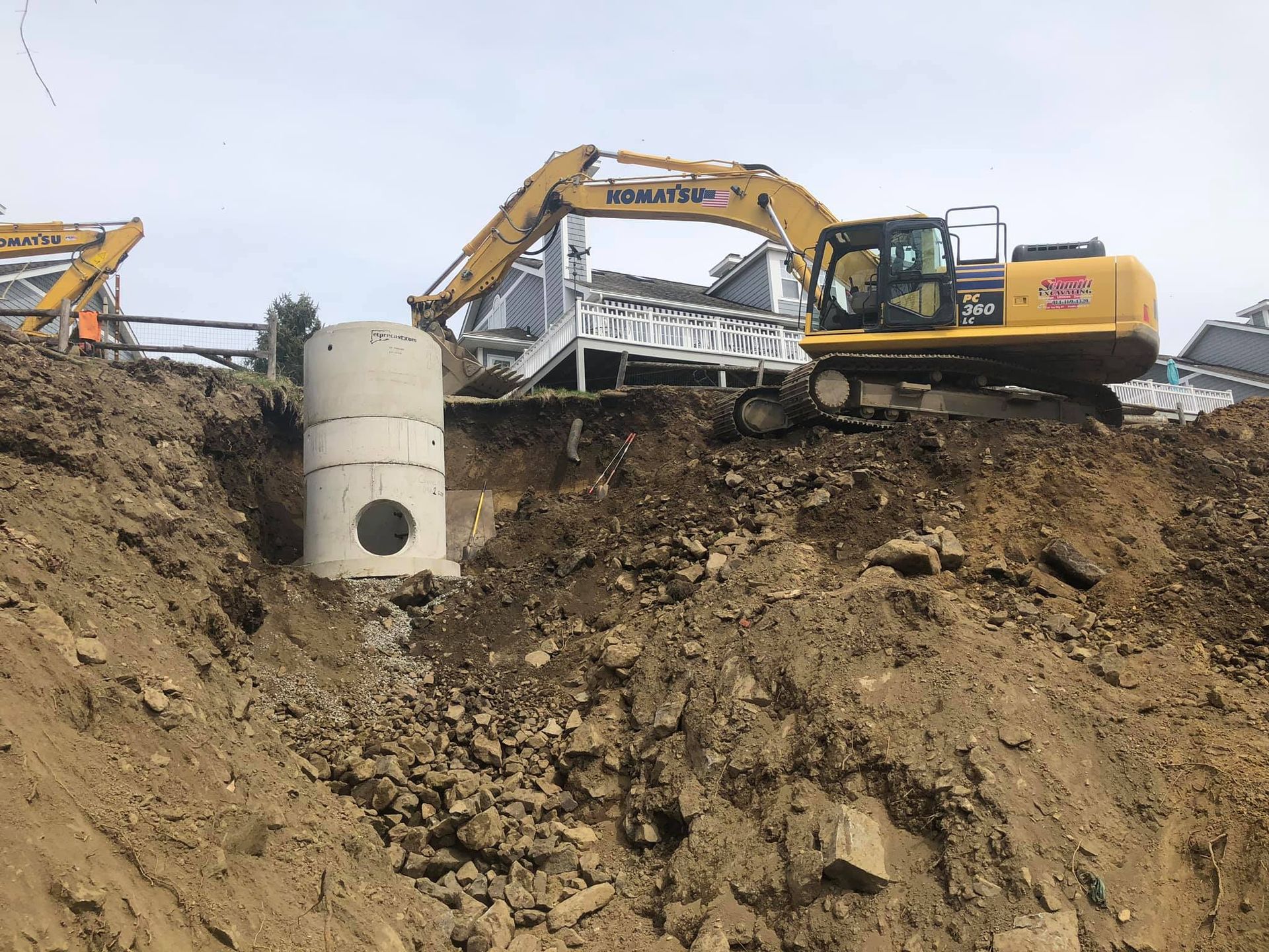 An excavator works near a concrete culvert on a dirt construction site.