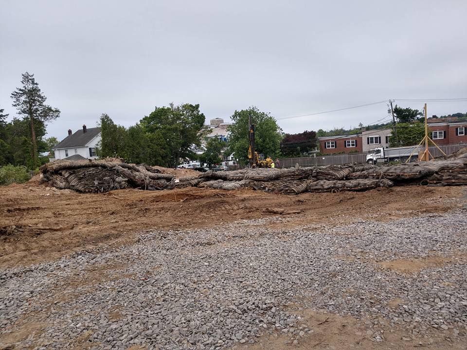 Construction site with piles of dirt and a small excavator, houses in background.