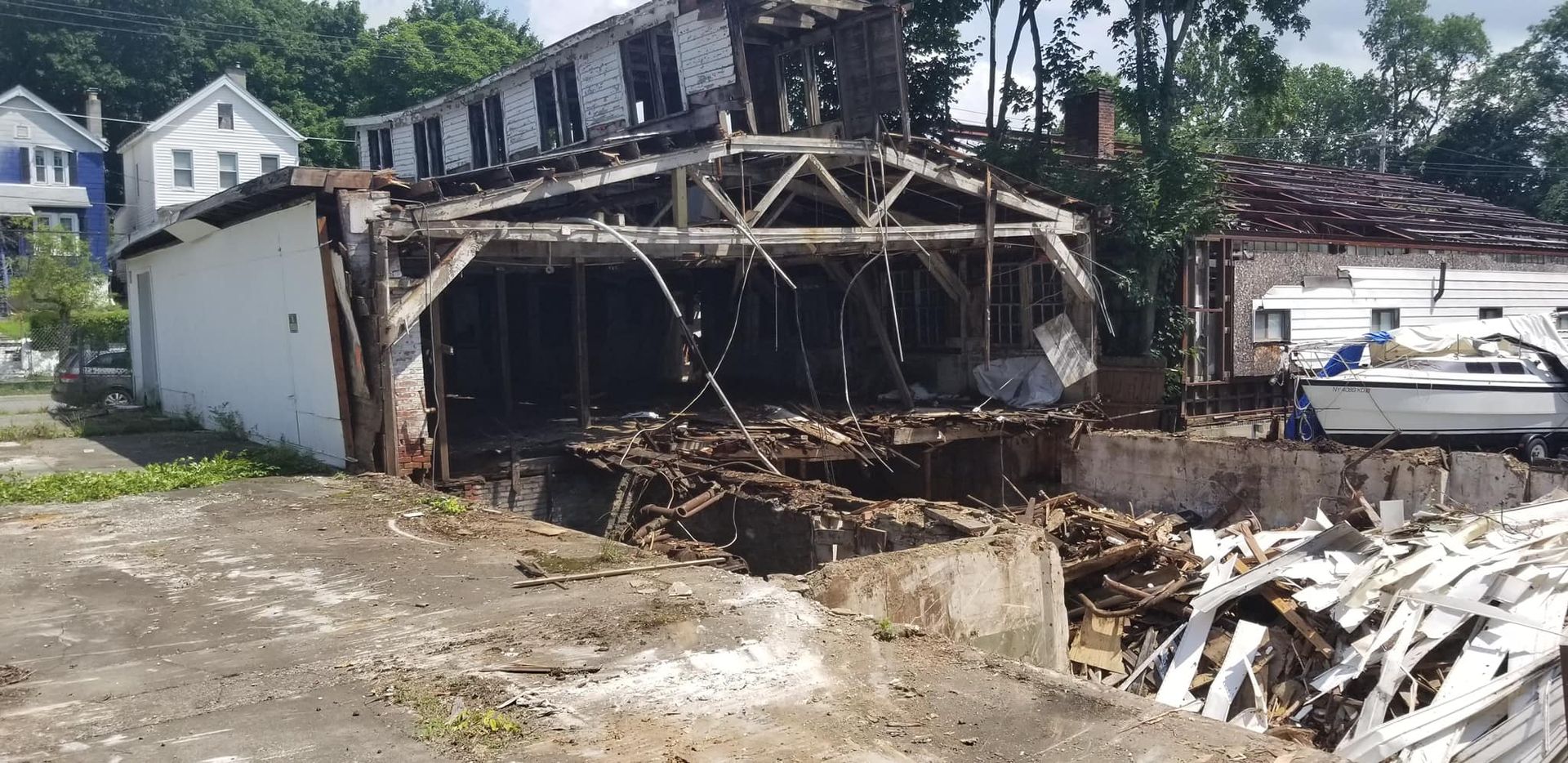 A dilapidated building with a partially collapsed roof, rubble, and a boat in the background.