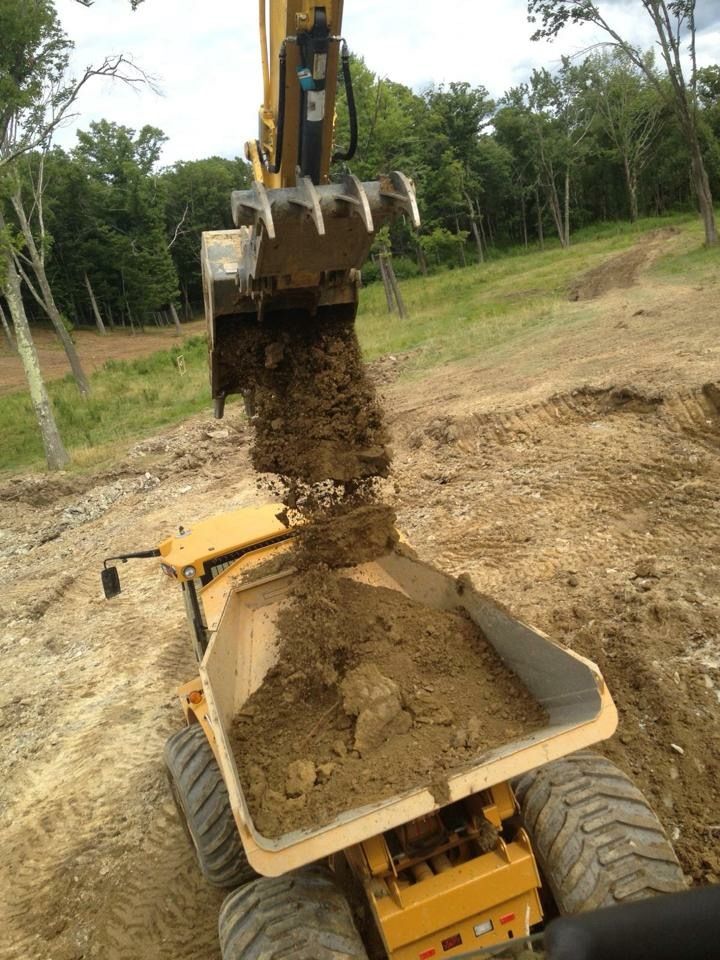 Yellow excavator dumping dirt into a yellow dump truck on a hillside.