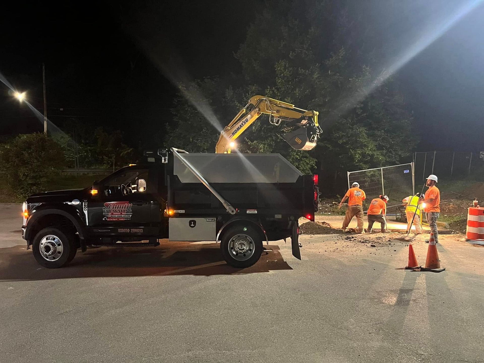 Construction site at night. Dump truck, excavator, and workers in safety vests.