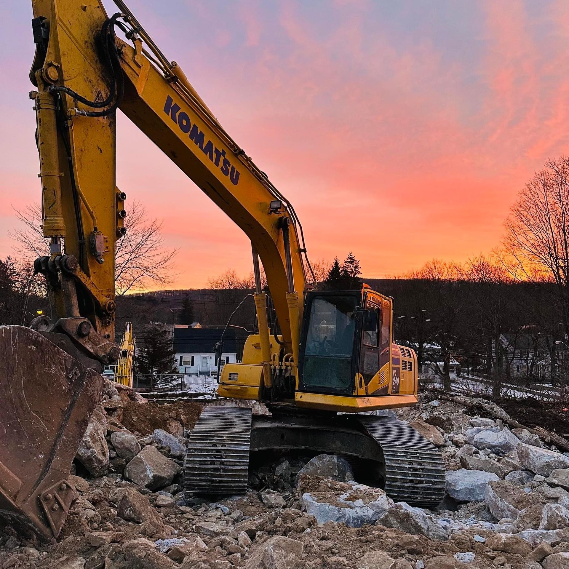 Yellow Komatsu excavator on demolition site, sunset sky.