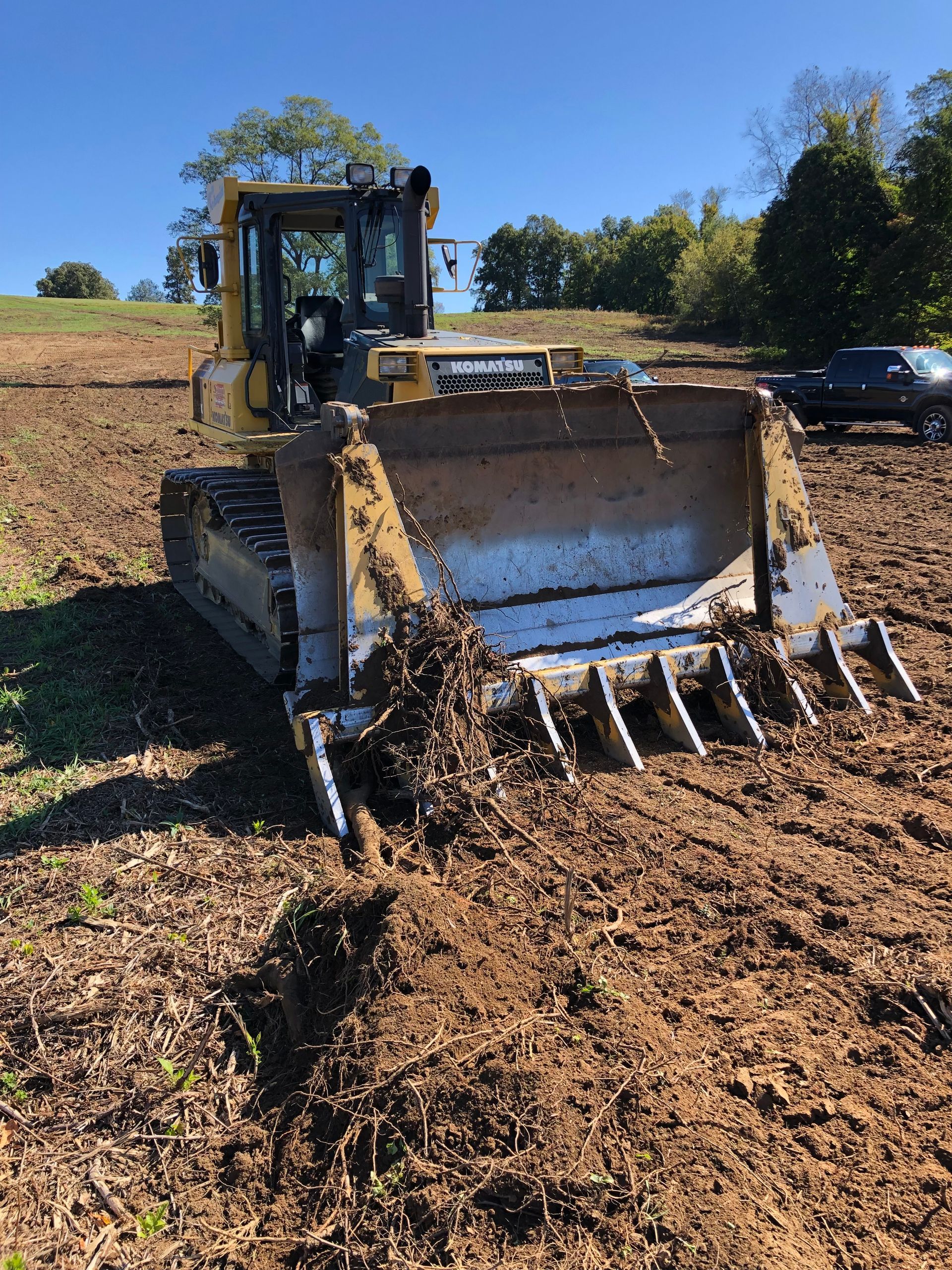 Yellow bulldozer on muddy ground, clearing debris in a field under a blue sky.