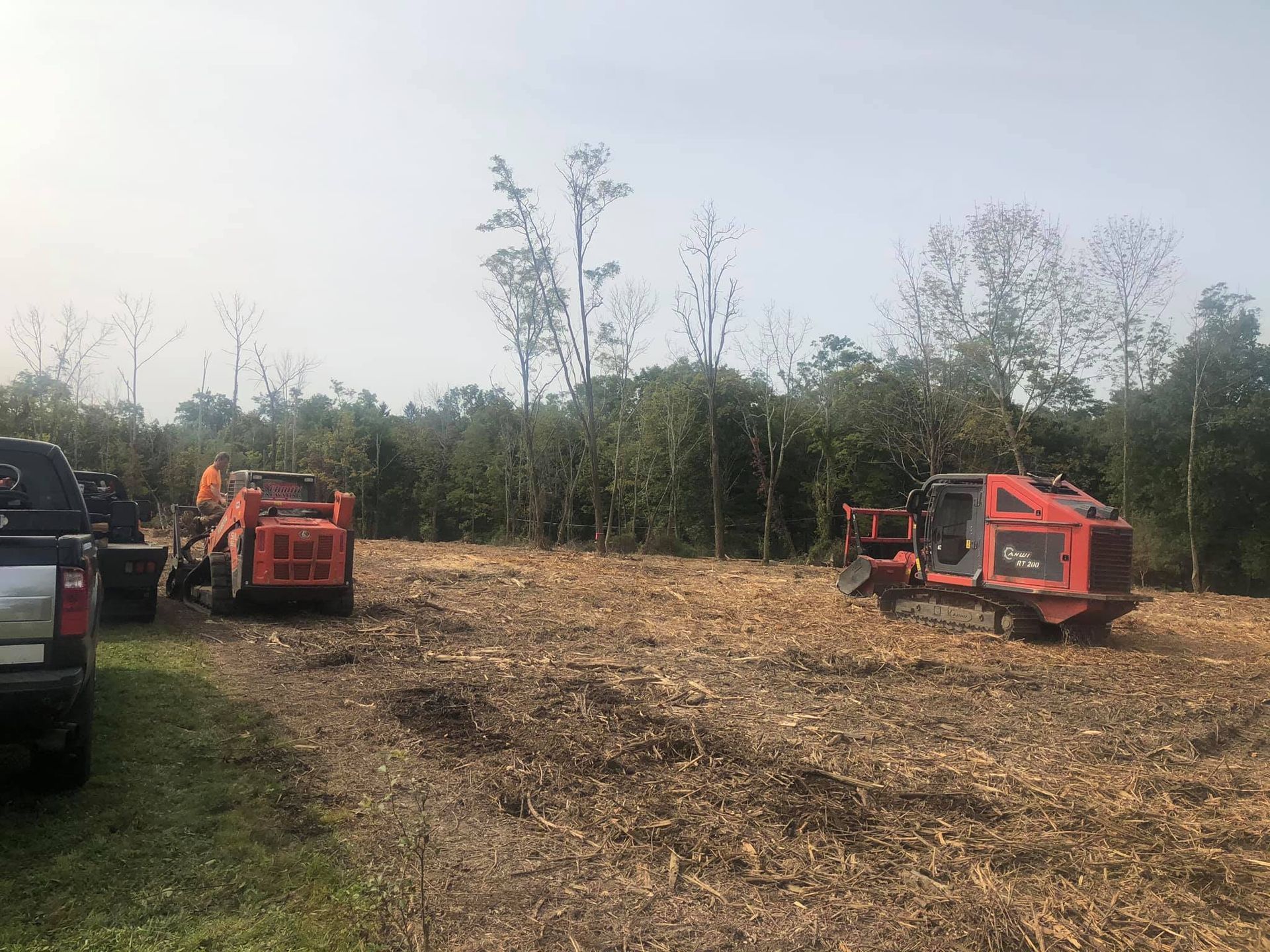 Two red machines and a truck clearing brush in a field.