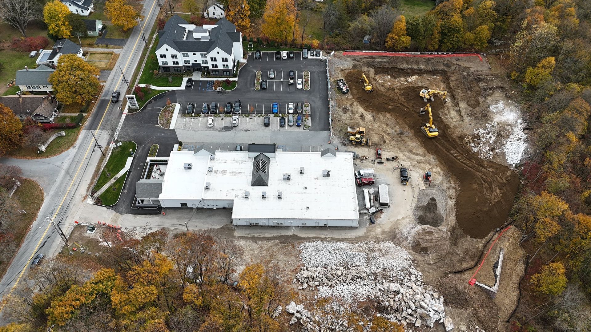Aerial view: construction site with large white building, heavy machinery, and surrounding trees.
