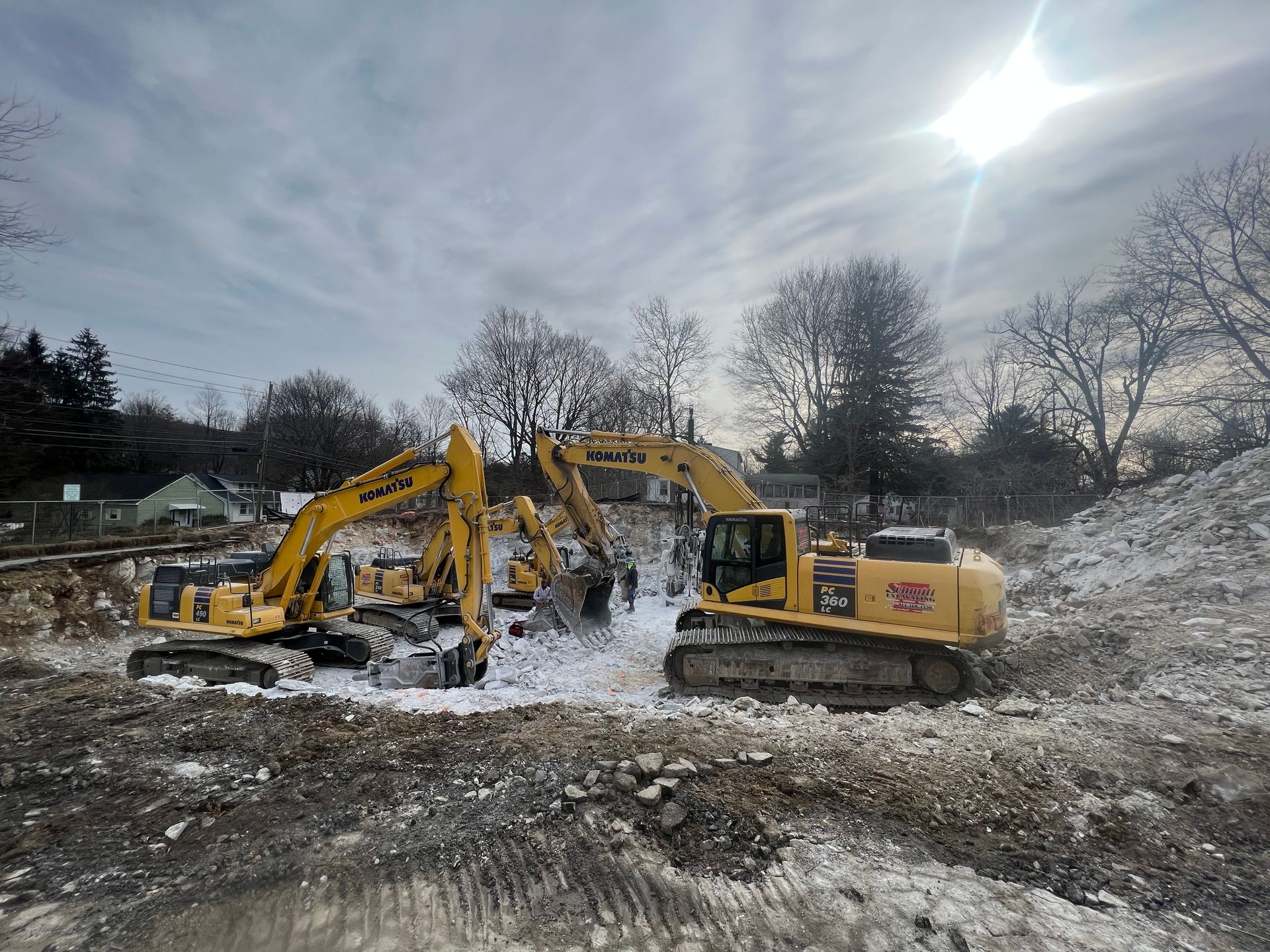 Three yellow excavators on a snowy construction site under a bright sun.