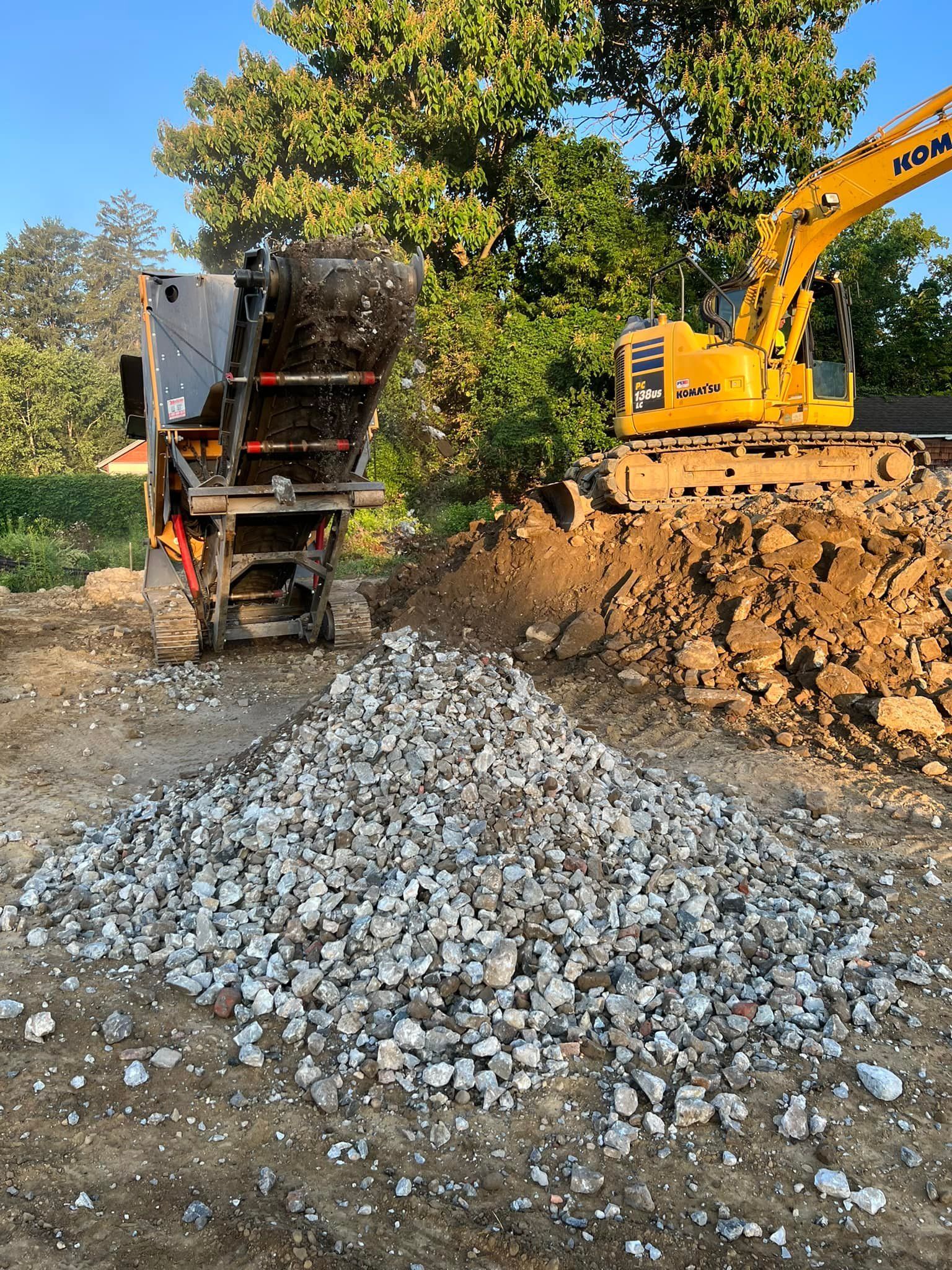 A pile of gravel with an excavator and a rock crusher on a construction site.