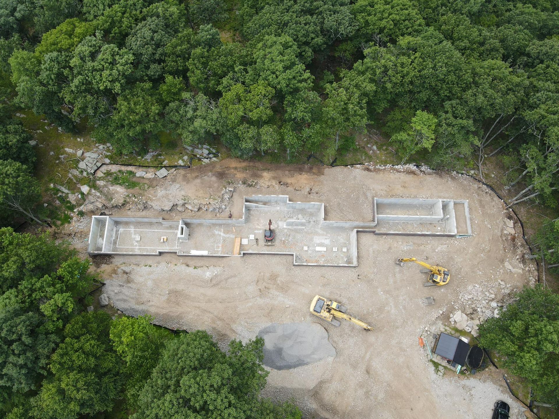Aerial view of a home's concrete foundation under construction; surrounded by trees and construction equipment.