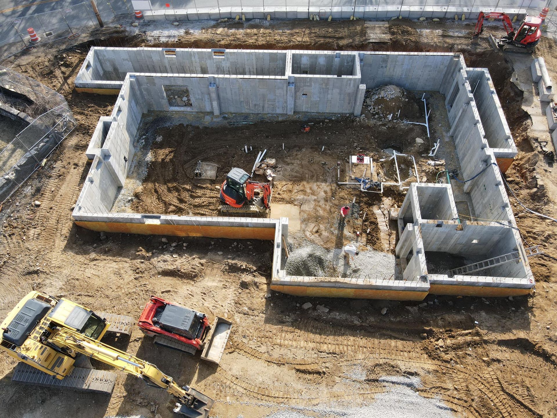 Construction site: concrete foundation walls with excavator machinery and dirt.