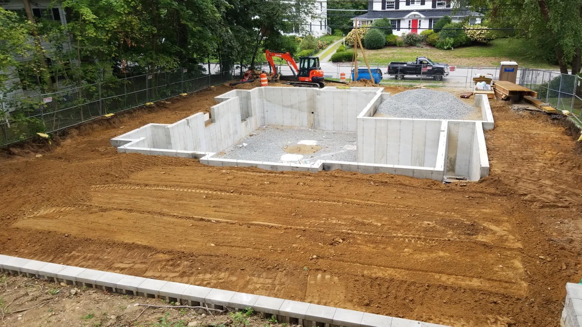 Construction site: Concrete foundation of a house surrounded by dirt and construction equipment.