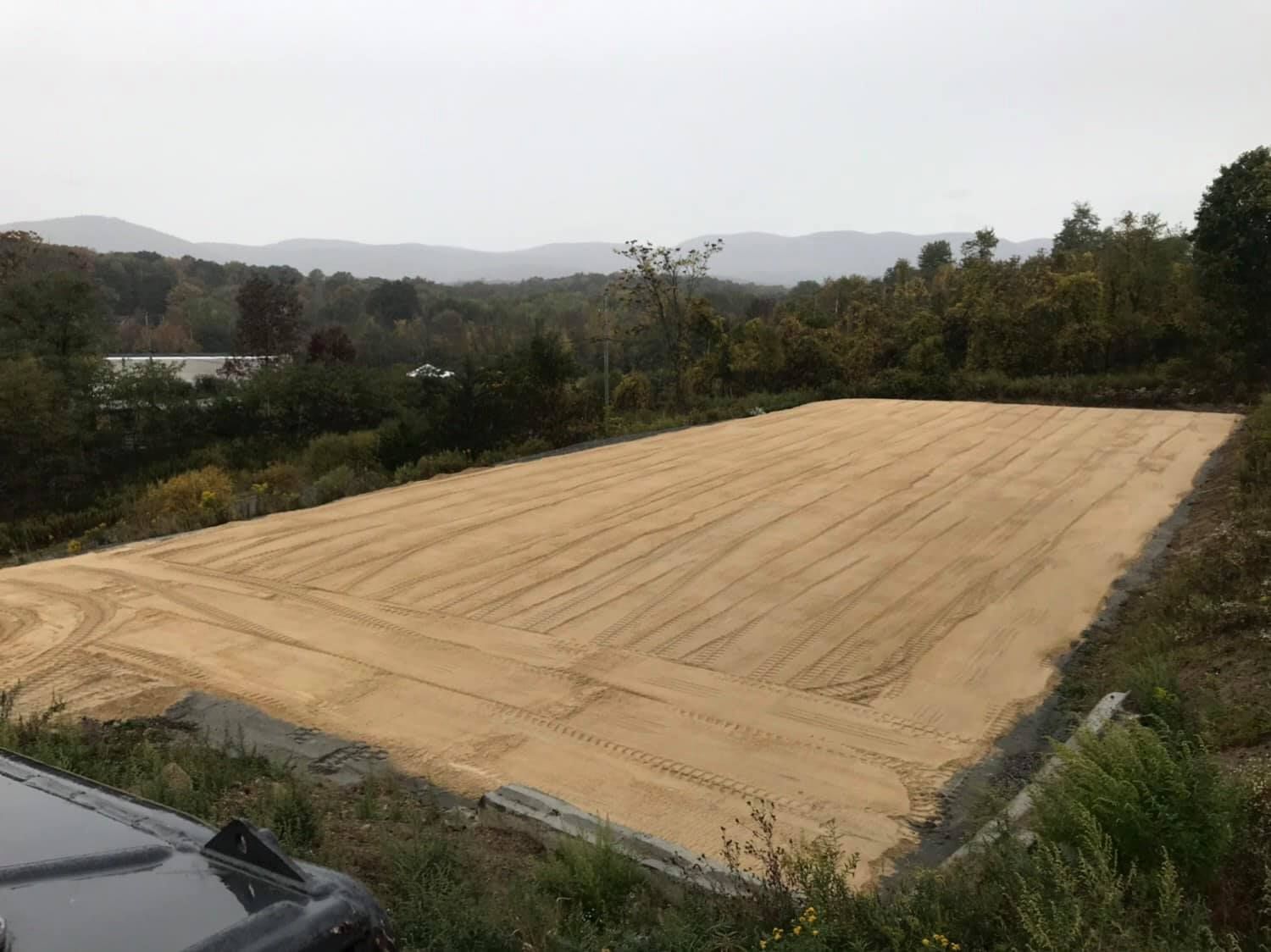 A rectangular sandy area, possibly a construction site, with a mountain backdrop.