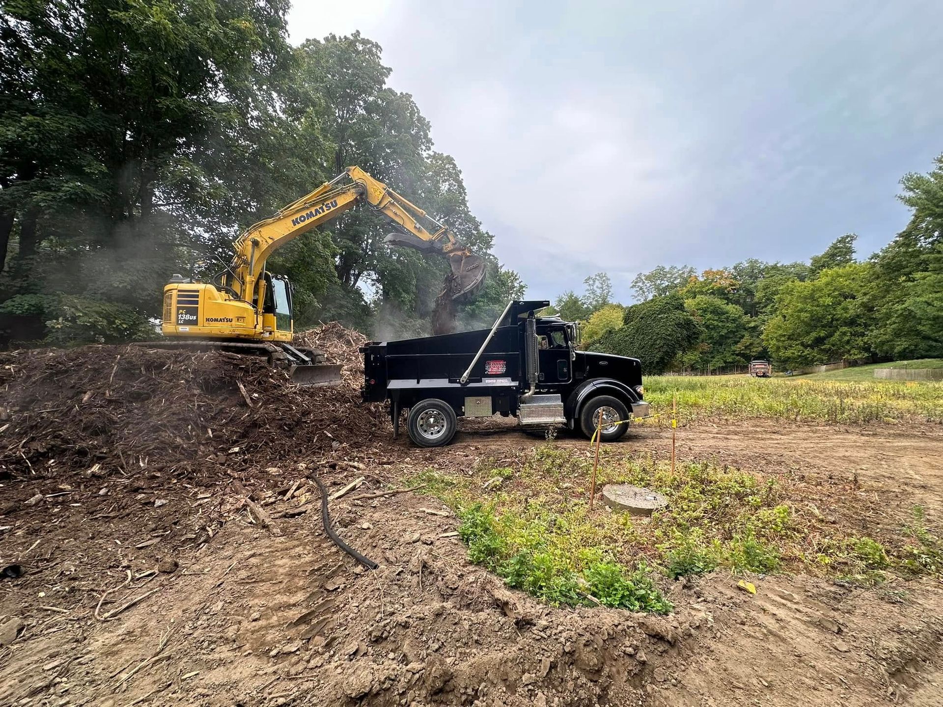 Yellow excavator loading dirt into a black dump truck at a construction site.