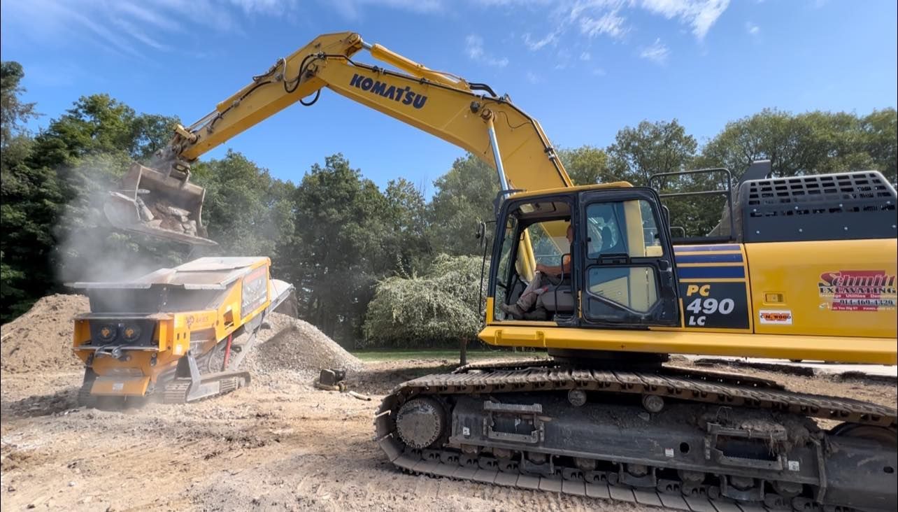 Yellow excavator loading material into a yellow screening machine outdoors.