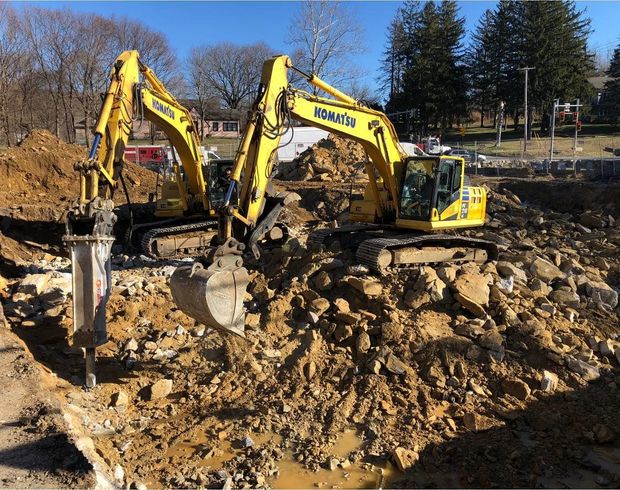 Two yellow Komatsu excavators work at a construction site, digging and breaking up soil.