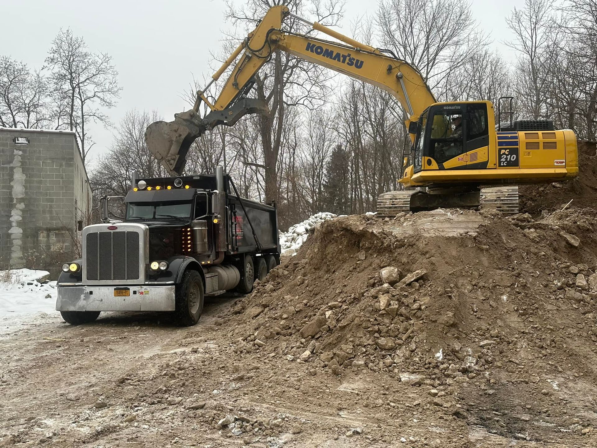 Yellow excavator loading dirt onto a black dump truck at a construction site.