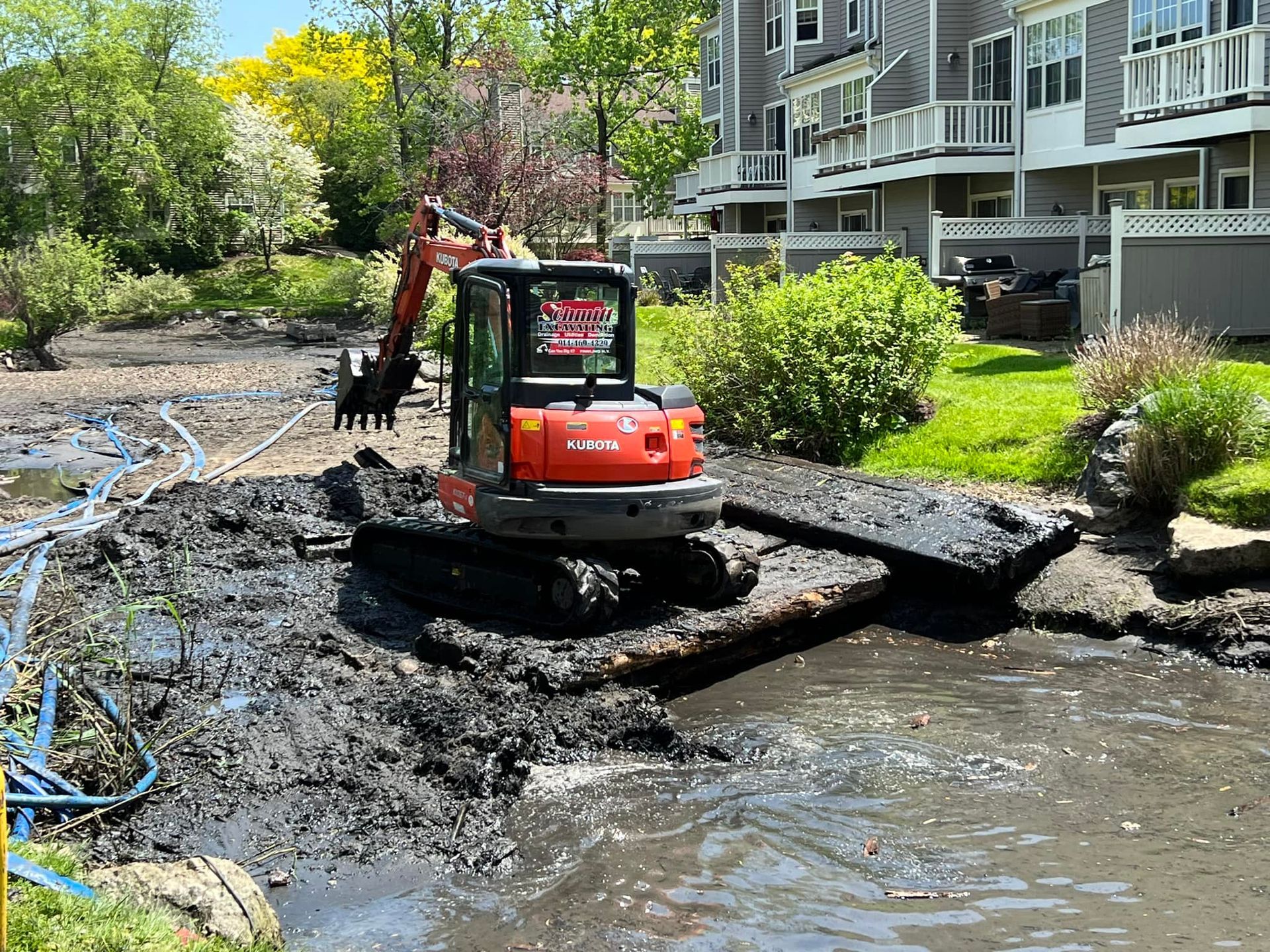 Mini excavator removing mud from a pond near a building.