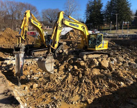Two yellow excavators digging in a muddy construction site under a clear sky