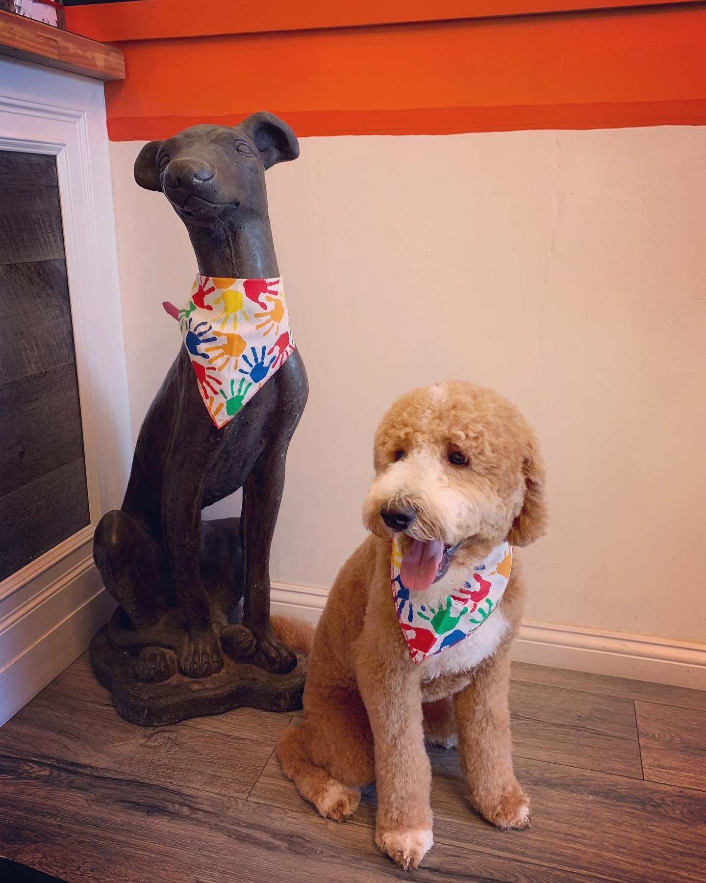 A dog wearing a bandana is sitting next to a statue of a dog.